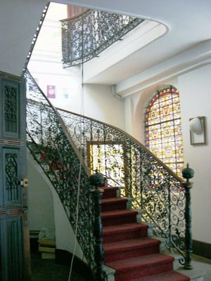 Escalier avec jolie rampe en fer forgé. Le vitrail à droite donne sur la cour vitrée.