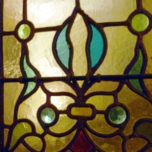 même type de fleur mais traitement différent (vers 1880). Éclairage électrique. Les vitraux sont attachés par des tourillons en plomb aux vergettes en fer solidaires de l'armature qui est fixée à l'encadrement, ici une porte en bois.