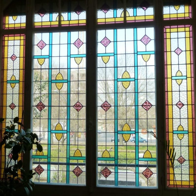 Le dormant de la verrière est en verre à relief, l'ouvrant au centre en verre lisse en dehors des motifs jaunes ou mauves.